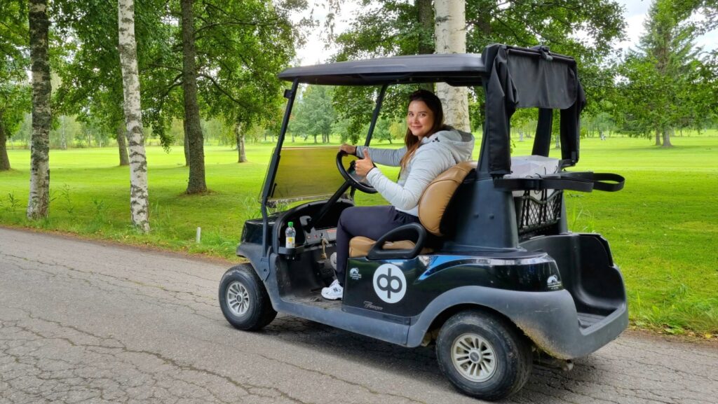 Kesätyöntekijä Kia-Emilia golf-auton ratissa peukkua näyttäen.