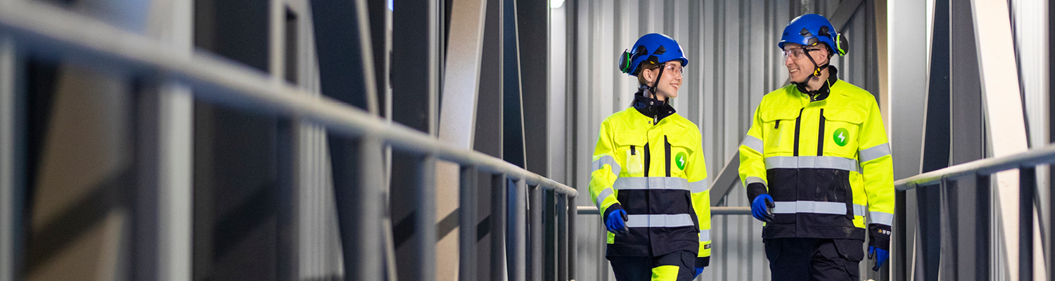 Kaksi Pori Energian työvarusteisiin pukeutunutta henkilöä kävelee Aittaluodon voimalaitoksen tiloissa ja katsoo toisiaan