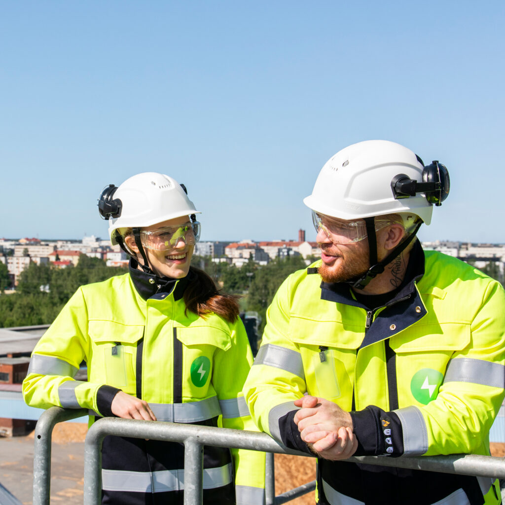 Kaksi Pori Energian työvarusteisiin pukeutunutta henkilöä seisoo korkealla tasanteella Aittaluodon voimalaitoksen ulkoympäristössä