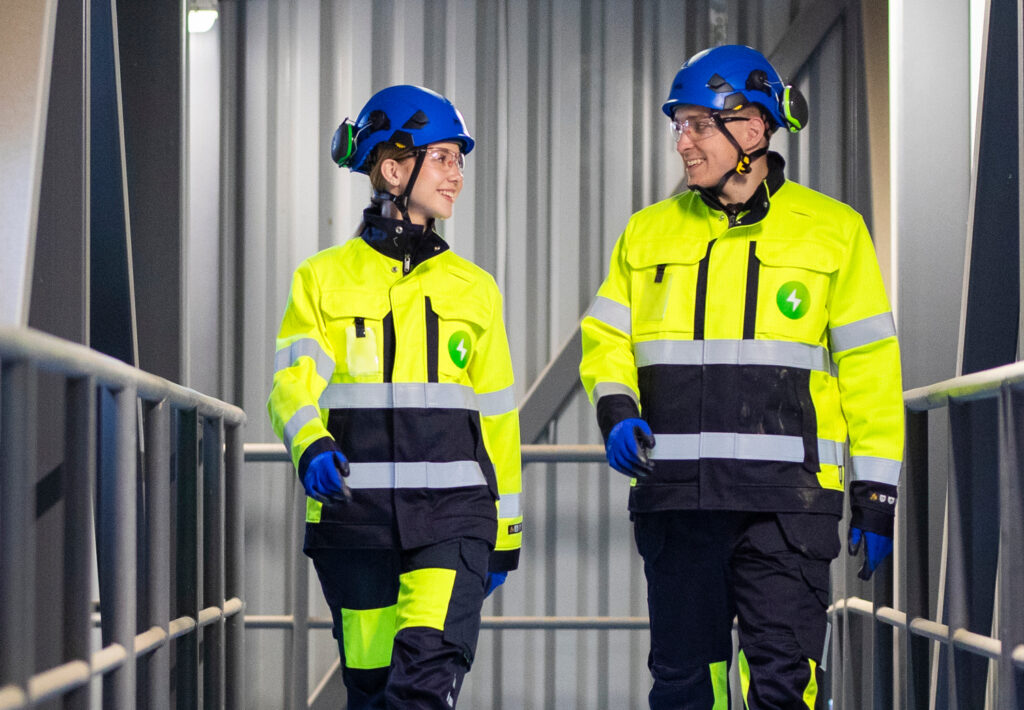 Kaksi Pori Energian työvarusteisiin pukeutunutta henkilöä kävelee Aittaluodon voimalaitoksen tiloissa ja katsoo toisiaan