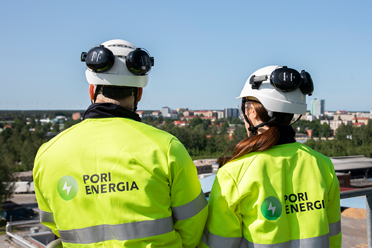Kaksi Pori Energian työvarusteisiin pukeutunutta henkilöä seisoo korkealla tasanteella Aittaluodon voimalaitoksen ulkoympäristössä selkä kameraan päin