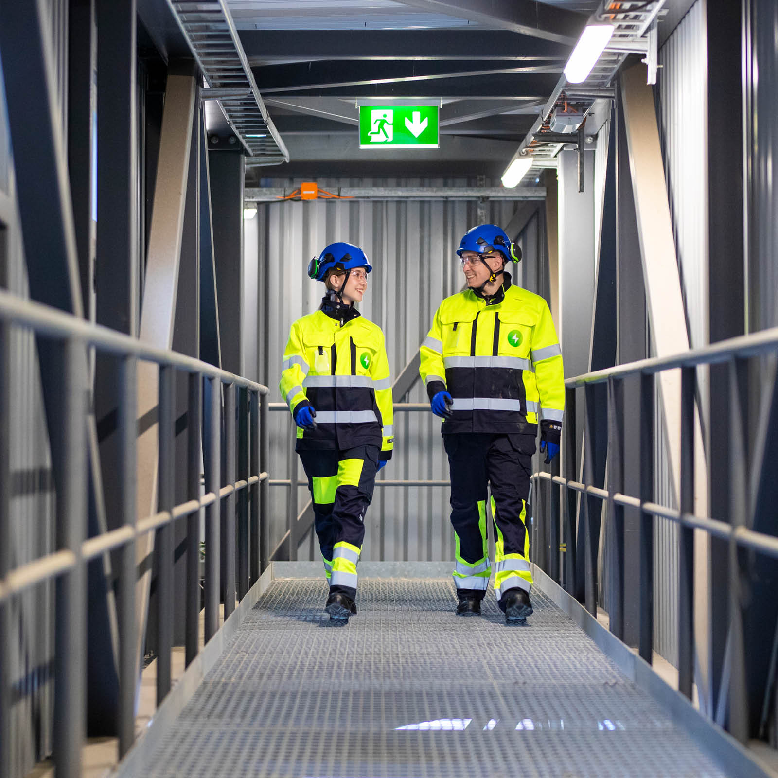 Kaksi Pori Energian työvarusteisiin pukeutunutta henkilöä kävelee Aittaluodon voimalaitoksen tiloissa ja katsoo toisiaan
