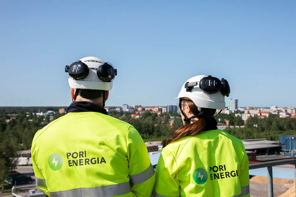 Kaksi Pori Energian työvarusteisiin pukeutunutta henkilöä seisoo korkealla tasanteella Aittaluodon voimalaitoksen ulkoympäristössä selkä kameraan päin