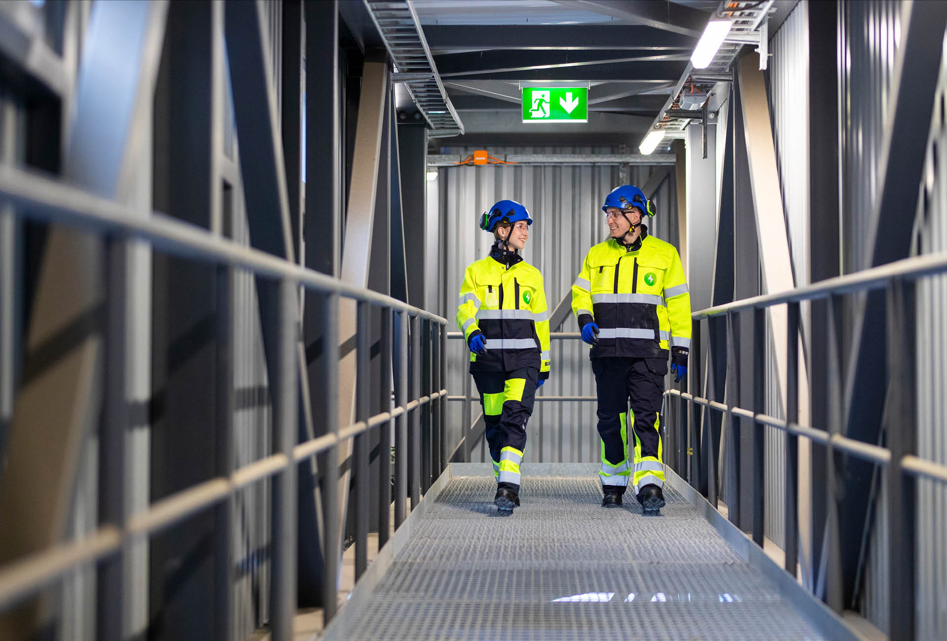 Kaksi Pori Energian työvarusteisiin pukeutunutta henkilöä kävelee Aittaluodon voimalaitoksen tiloissa ja katsoo toisiaan